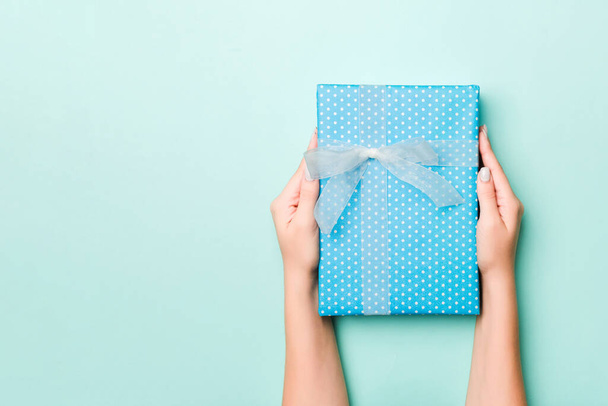 Γυναικεία χέρια δώσει τυλιγμένο Χριστούγεννα ή άλλα χειροποίητα δώρα διακοπών σε χρωματιστό χαρτί. Παρόν κουτί, διακόσμηση δώρου σε μπλε τραπέζι, πάνω όψη με χώρο αντιγραφής. - Φωτογραφία, εικόνα