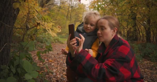 mère caucasienne et bébé reposent dans la forêt et regardent des photos sur smartphone, photographie mobile de la nature - Séquence, vidéo