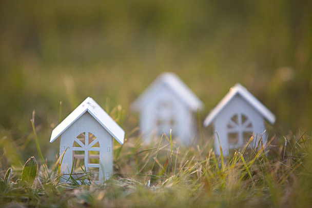Postavy malých bílých dřevěných domků na trávě zblízka. Chalupa se nachází ve venkovské lokalitě a obci, budova, projekt, stěhování, hypotéka, pronájem a nákup nemovitostí. Kopírovat prostor - Fotografie, Obrázek