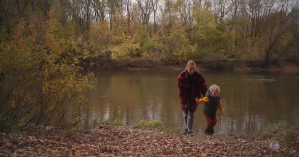 casual στυλ ρούχα για τη μητέρα και το παιδί για το περπάτημα στη φύση και την ενεργό ανάπαυση, γυναίκα και αγόρι περπατούν στην ακτή της λίμνης - Πλάνα, βίντεο