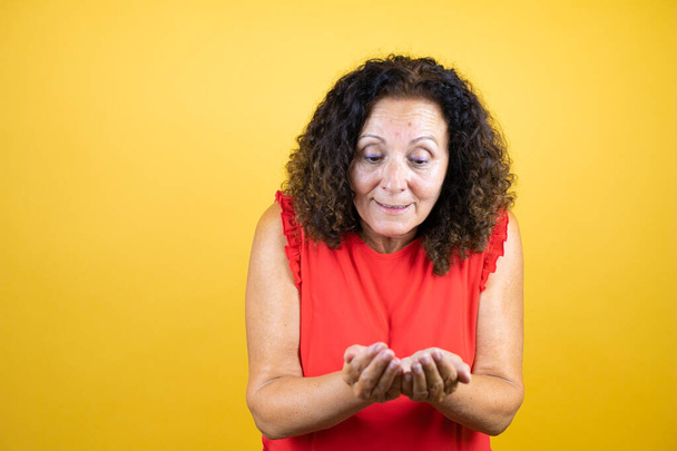 Žena středního věku v ležérní košili stojící nad izolovaným žlutým pozadím Usmívající se dlaněmi k sobě přijímá nebo gestikuluje. Držet a chránit - Fotografie, Obrázek