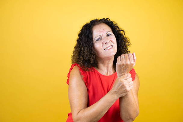 Middle age woman wearing casual shirt standing over isolated yellow background suffering pain on hands and fingers, arthritis inflammation - Фото, изображение