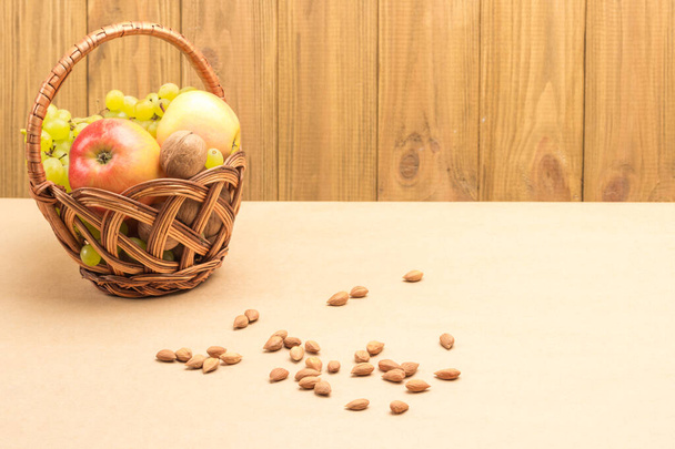 Wicker basket with fruits and nuts. Nuts are scattered on table. Brown background. Top view. Copy space - Foto, Imagen