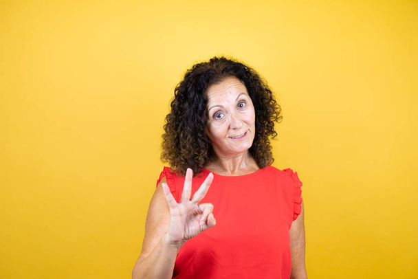 Keski-ikäinen nainen päällään rento paita seisoo yli eristetty keltainen tausta osoittaa ylös sormet numero kolme hymyillen itsevarma ja onnellinen - Valokuva, kuva
