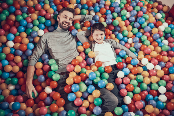 Dad and son look at camera while lying in balls. - Valokuva, kuva