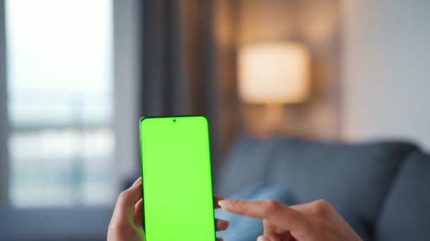 Woman at home lying on a sofa and using smartphone with green mock-up screen in vertical mode. Girl browsing Internet, watching content, videos, blogs. POV. - Кадры, видео
