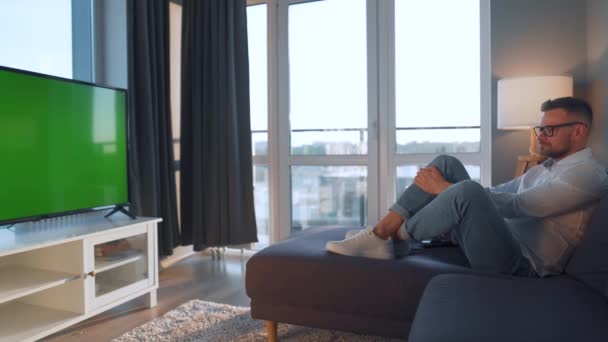 Férfi otthon fekszik a kanapén, és TV-t néz zöld makett képernyő - Felvétel, videó