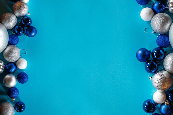 Shiny Christmas balls in blue, white and silver are arranged in a row on a turquoise background with a space for text. - Foto, Imagen