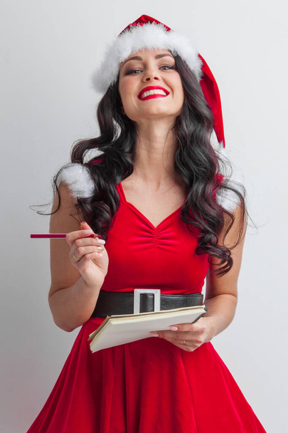 Pretty smiling pin-up Santa girl with wish list letter and red pencil - Фото, изображение