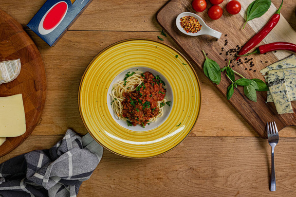 Espaguetis tradicionales italianos boloñeses en una mesa de madera con ingredientes al lado.  - Foto, imagen