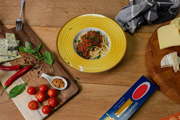 Bolonhesa tradicional de espaguete italiano em uma mesa de madeira com ingredientes ao lado dela.Vista superior  - Foto, Imagem
