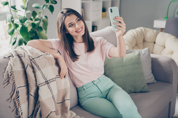 Photo portrait of young girl taking selfie with mobile phone sitting on couch with legs crossed indoors - Foto, immagini