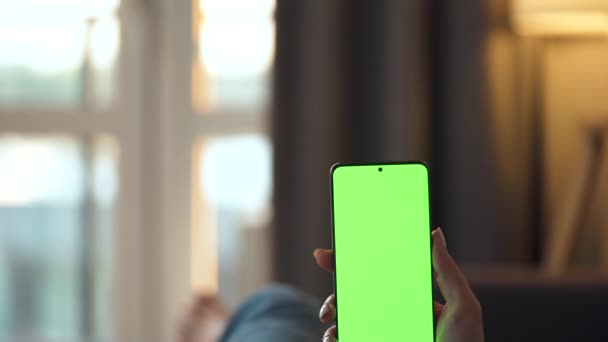 Kobieta w domu leży na kanapie i używa smartfona z zielonym ekranem makiety w trybie pionowym. Dziewczyna przeglądająca Internet, oglądająca treści, filmy, blogi. POV. - Materiał filmowy, wideo