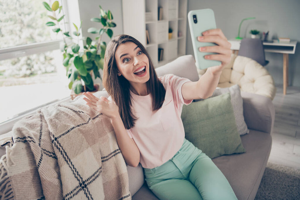 Photo portrait of woman video calling waving hand smiling with open mouth holding phone in hand indoors - 写真・画像