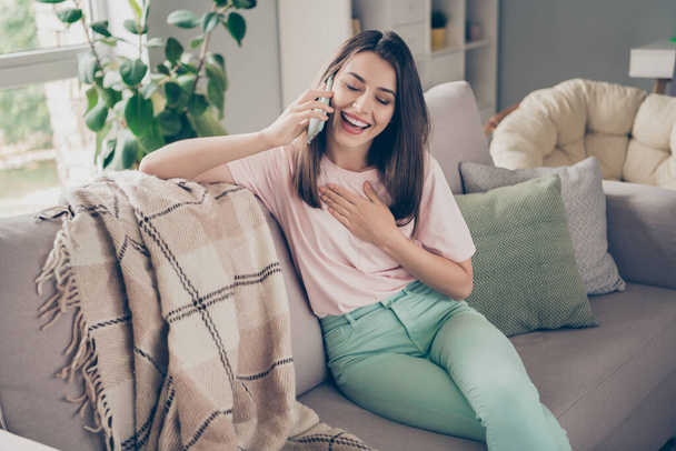 Photo portrait of woman talking on phone touching chest laughing sitting on sofa indoors - Foto, Imagem
