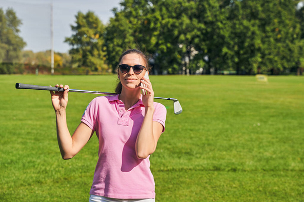Smiling female with a golf club calling on her cellphone - Фото, изображение