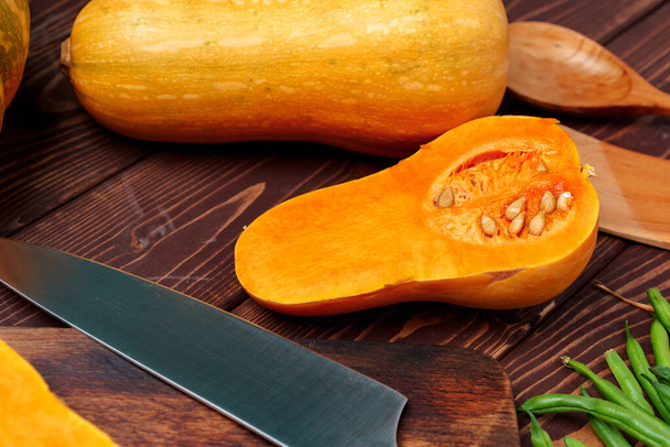 Small pumpkin cut into halves on wooden cutting board with knife - Фото, изображение