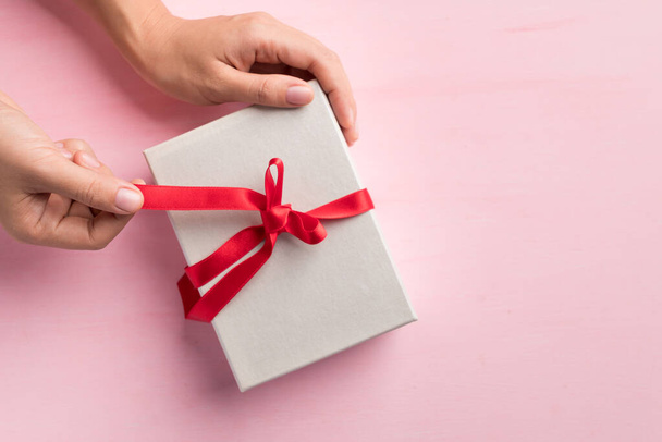 Kadın eli kırmızı kurdeleyle süslenmiş kağıt hediye kutusu, özel gün için hediye paketi, Top view - Fotoğraf, Görsel