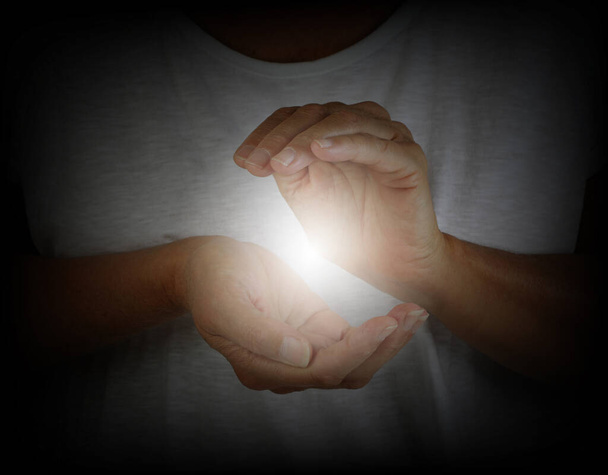 Healer demonstrating how to sense the human electromagnetic with hands - woman in a white top with hands cupped around a white ball of energy  - Photo, Image