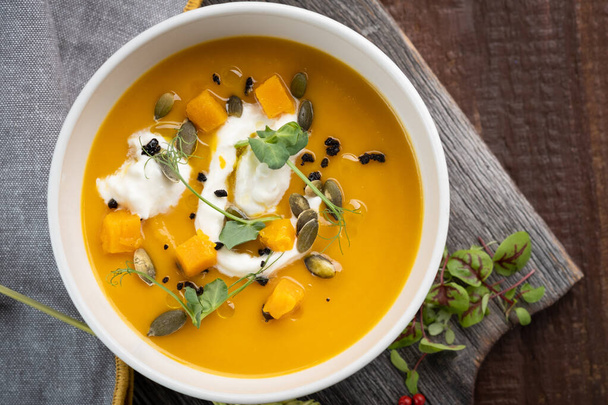 Pumpkin cream soup with seeds and herbs in a white bowl on a wooden background, top view and rustic style - Foto, Imagem