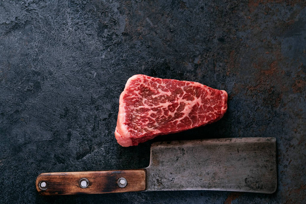 Roh marmoriertes Steak vom Schulterblatt-Rindfleisch mit einem Fleischspalter auf dunklem Hintergrund - Foto, Bild