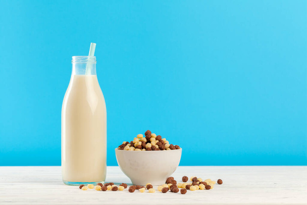 Breakfast cereal balls and milk in glass against blue background - 写真・画像