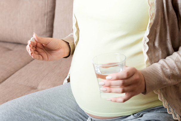 Terhes nő ül a kanapén. Gyógyszert szed a megfázástól. A terhesség utolsó hónapjai. - Fotó, kép