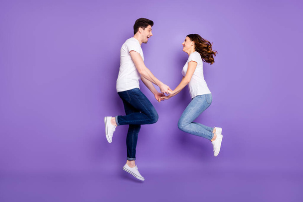 Full size profile side photo romance affectionate passionate couple man woman jump hold hand enjoy weekend rest wear casual style outfit white footwear isolated purple color background - Foto, immagini