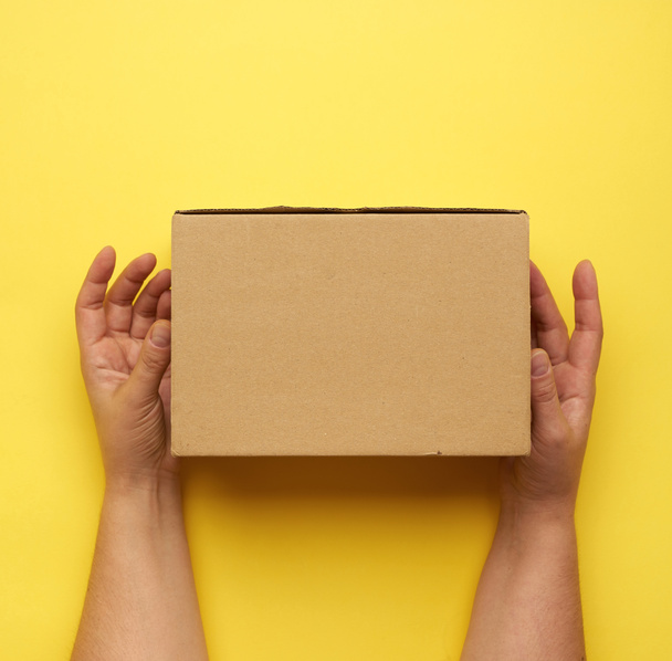 two female hands hold closed paper box on a yellow background, top view - Photo, Image