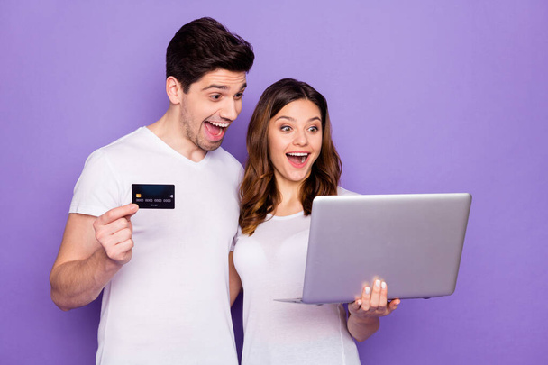 Photo pretty lady handsome guy couple hold notebook spend free time together use plastic wireless credit card online transfer buy delivery food wear t-shirts isolated purple color background - 写真・画像
