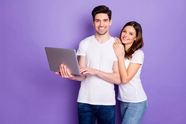 Portrait of positive couple man woman hold laptop work from home have online partnership communication wear white t-shirt casual style denim jeans isolated over violet color background - Photo, Image