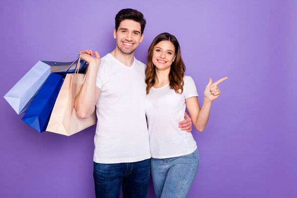 Photo pretty lady handsome guy couple good mood go shopping together hold many store package spree direct finger empty space wear casual t-shirts jeans isolated purple color background - Fotografie, Obrázek