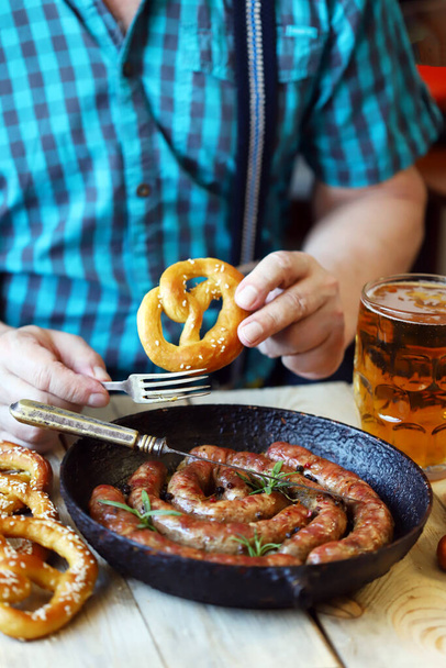A man in a bar eats sausages and pretzels with beer. Oktoberfest menu. - Photo, Image