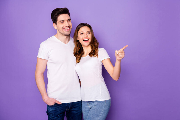 Positive married couple students summer rest relax look indicate advert promo girl point index finger copyspace wear white casual style clothes denim jeans isolated violet color background - Foto, immagini