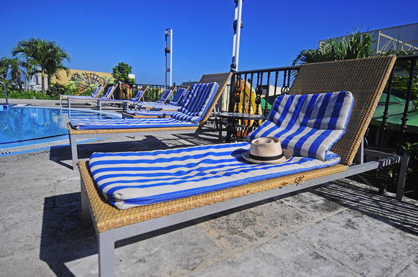 View of striped long deck chairs set by swimming-pool - Photo, Image
