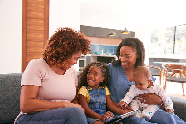 Multi-Generation Female African American Family Sitting On Sofa At Home Using Digital Tablet - Foto, afbeelding
