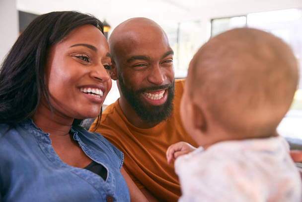 Sorrindo os pais afro-americanos abraçando e brincando com a filha do bebê dentro de casa no sofá - Foto, Imagem