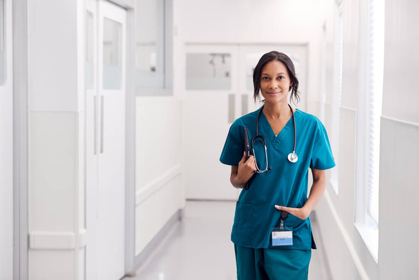 Retrato de la sonriente doctora usando exfoliantes en el pasillo del hospital sosteniendo la tableta digital - Foto, imagen
