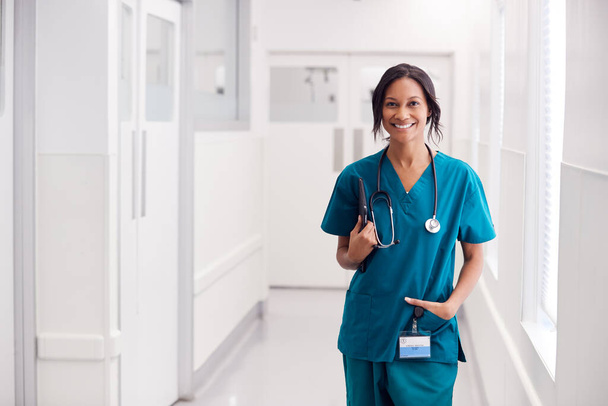 Portrait Of Smiling Female Doctor Wearing Scrubs In Hospital Corridor Holding Digital Tablet - Φωτογραφία, εικόνα