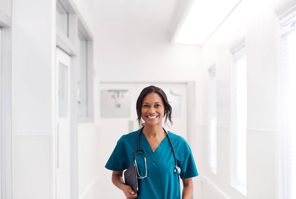 Portrait Of Smiling Female Doctor Wearing Scrubs In Hospital Corridor Holding Digital Tablet - Foto, Imagem