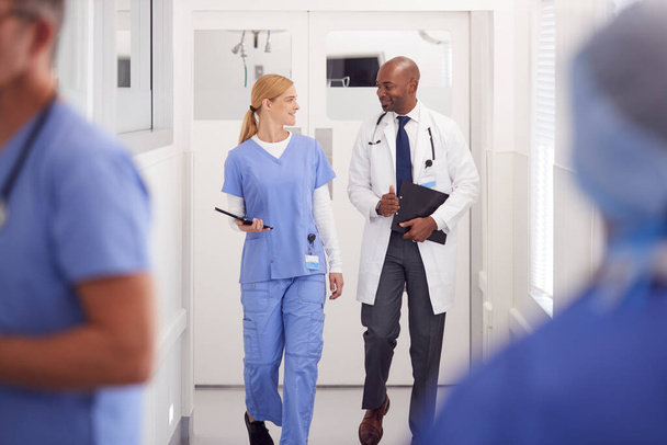 Médico con bata blanca y enfermera con exfoliantes discutiendo en el pasillo del hospital - Foto, imagen