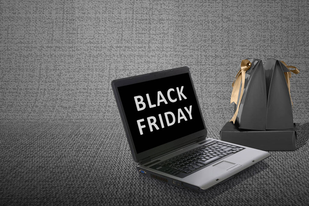 Black paper bag with a gold ribbon with a laptop with Black Friday promotion. Black Friday concept - Foto, afbeelding