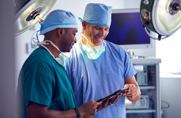 Male Surgeons Wearing Scrubs Looking At Digital Tablet In Hospital Operating Theater - Фото, зображення