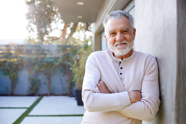 Portrait Of Smiling Retired Senior Hispanic Man In Garden At Home Against Flaring Sun - Foto, imagen