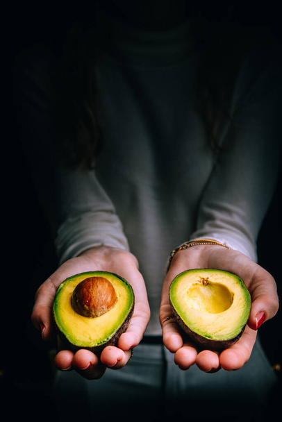 Veganistisch eten. Gesneden avocado in vrouwelijke handen.  - Foto, afbeelding