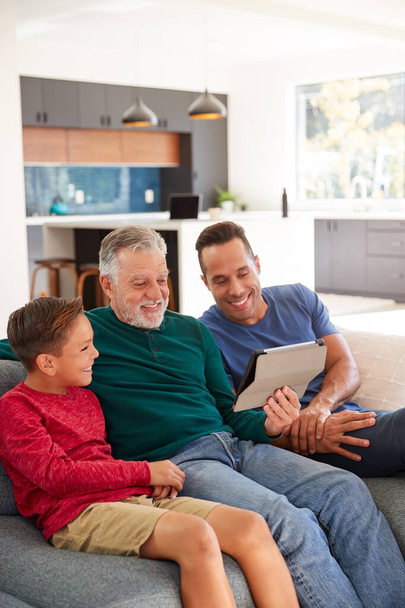 Multi-Generation Male Hispanic Family Sitting On Sofa At Home Watching Movie On Digital Tablet - Fotografie, Obrázek