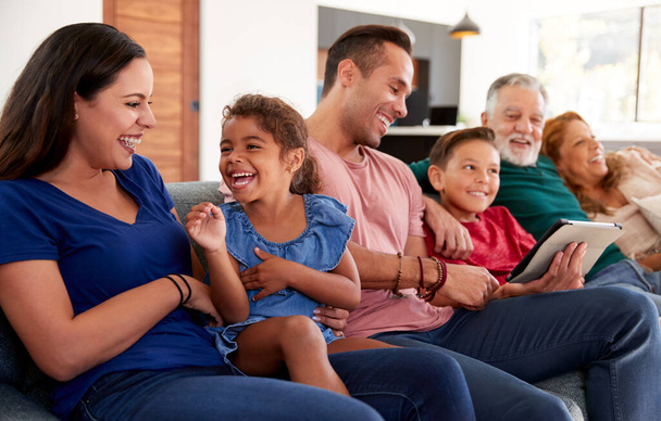 Multi-Generation Hispanic Family Relaxing On Sofa As Grandson Plays With Digital Tablet - Valokuva, kuva