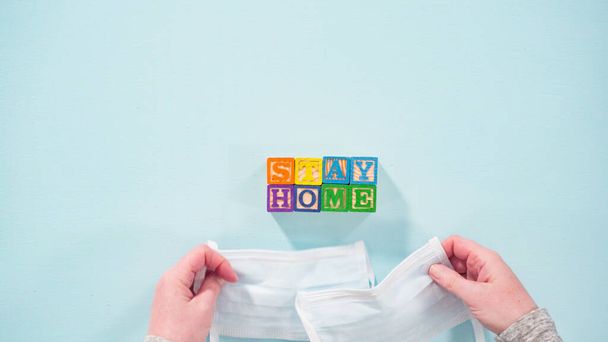 Plat gelegd. STAY HOME uithangbord uit alfabet blokken voor kinderen met zelfgemaakte gezichtsmaskers op een witte achtergrond. - Foto, afbeelding