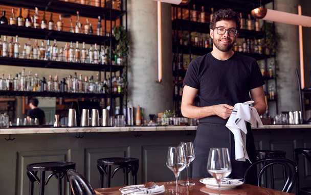 Portrait Of Male Waiter Polishing Glasses Before Service In Bar Restaurant - Фото, изображение