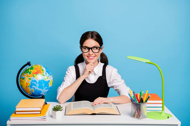 Photo minded girl university student sit table read textbook think thoughts touch hand chin look copyspace wear white blouse black overall ponytails uniform isolated blue color background - Foto, Imagen